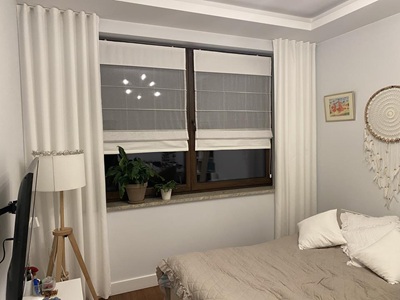 Modernes Schlafzimmer mit cremefarbenen Vorh&auml;ngen und transparenten Raffrollos